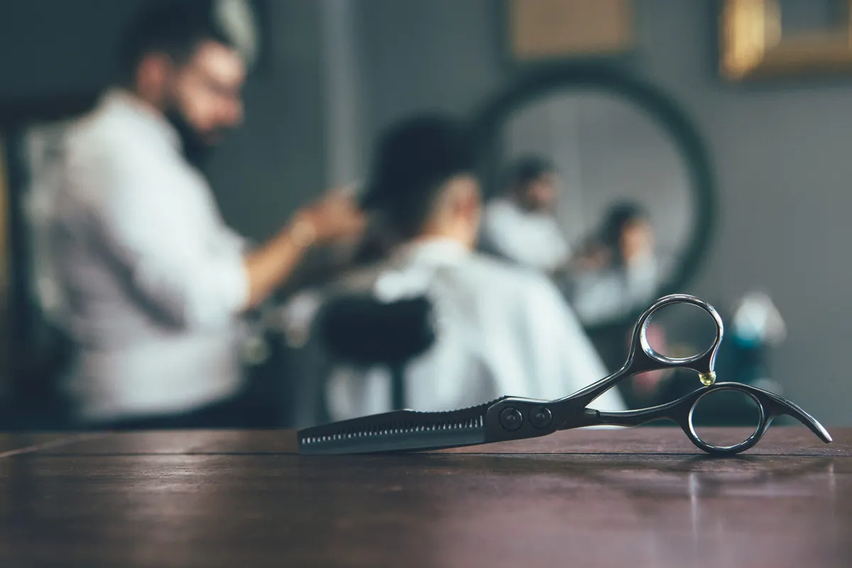 Schere auf dem Tisch, im Hintergrund ein Mann beim Haarschnitt