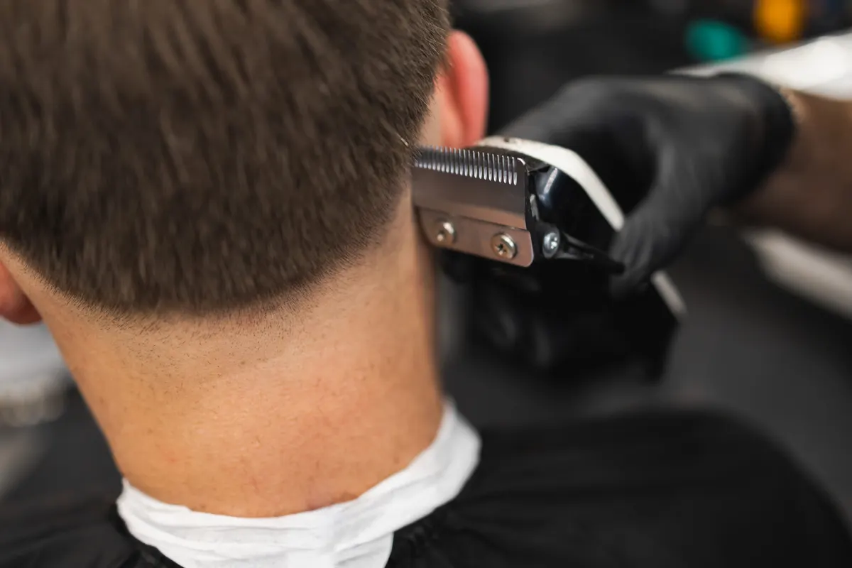 Friseur schneidet einem Mann die Haare mit der Haarschneidemaschine