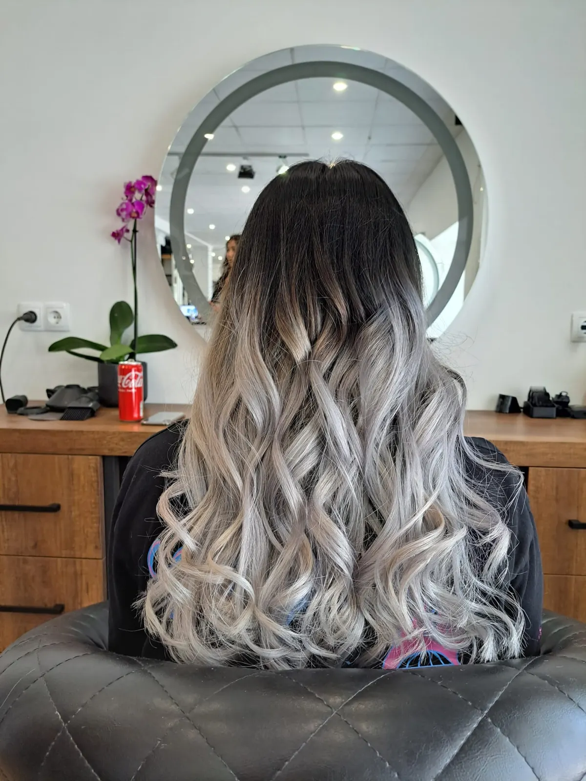 Kundin mit silberner Balayage vor dem runden Spiegel im Salon